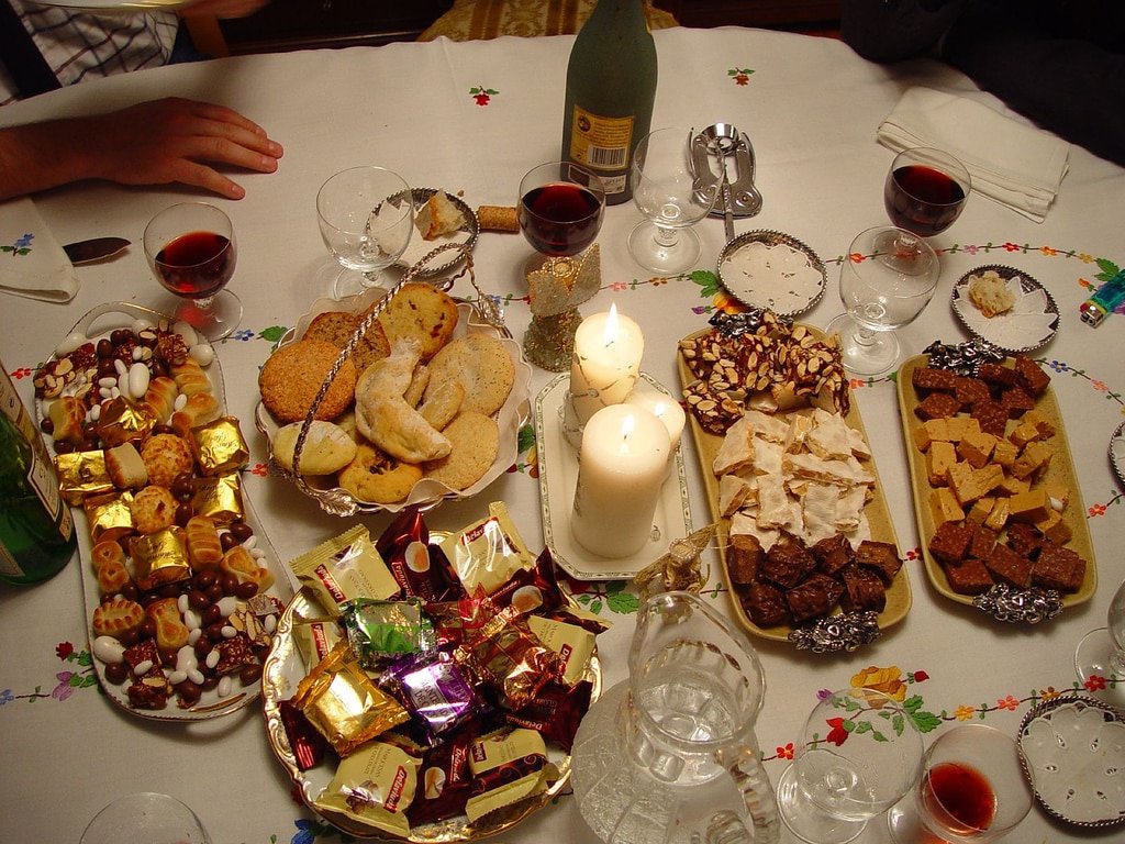 Spanish Christmas table with turrón, polvorones, mantecados, assorted chocolates, nuts, wine glasses, and candles.